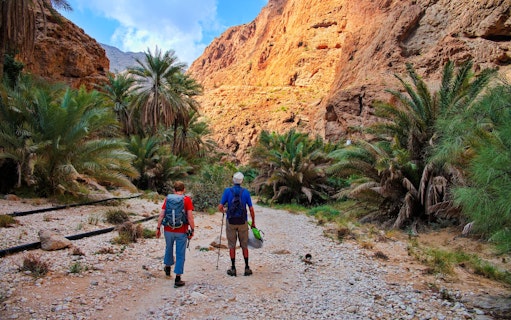 Couple hiking through rocky path surrounded by palm trees in Wadi Shab, Oman.