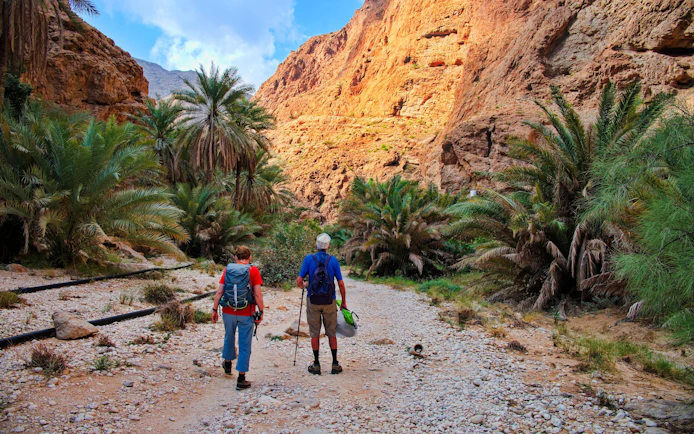 Couple hiking through rocky path surrounded by palm trees in Wadi Shab, Oman.