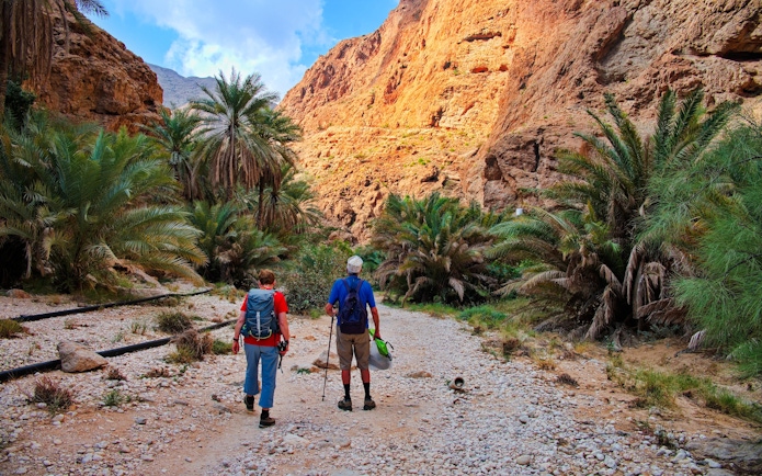 Couple hiking through rocky path surrounded by palm trees in Wadi Shab, Oman.