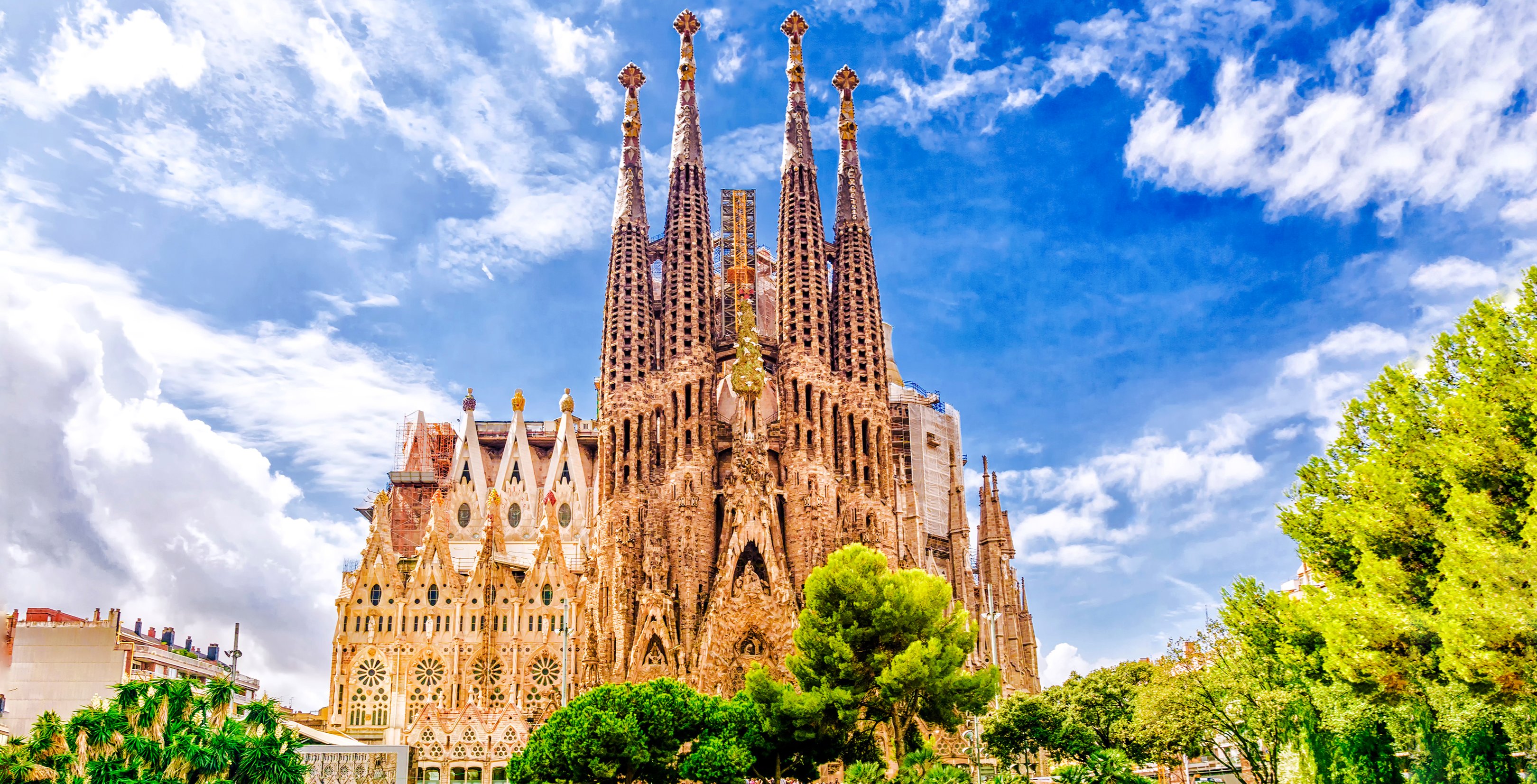 Sagrada Familia basilica with intricate spires in Barcelona, surrounded by trees under a blue sky.
