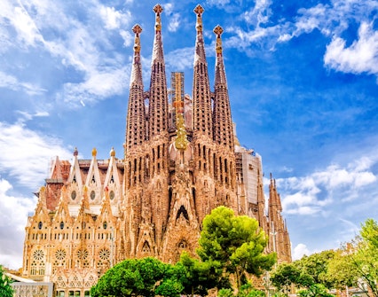 Sagrada Familia basilica with intricate spires in Barcelona, surrounded by trees under a blue sky.