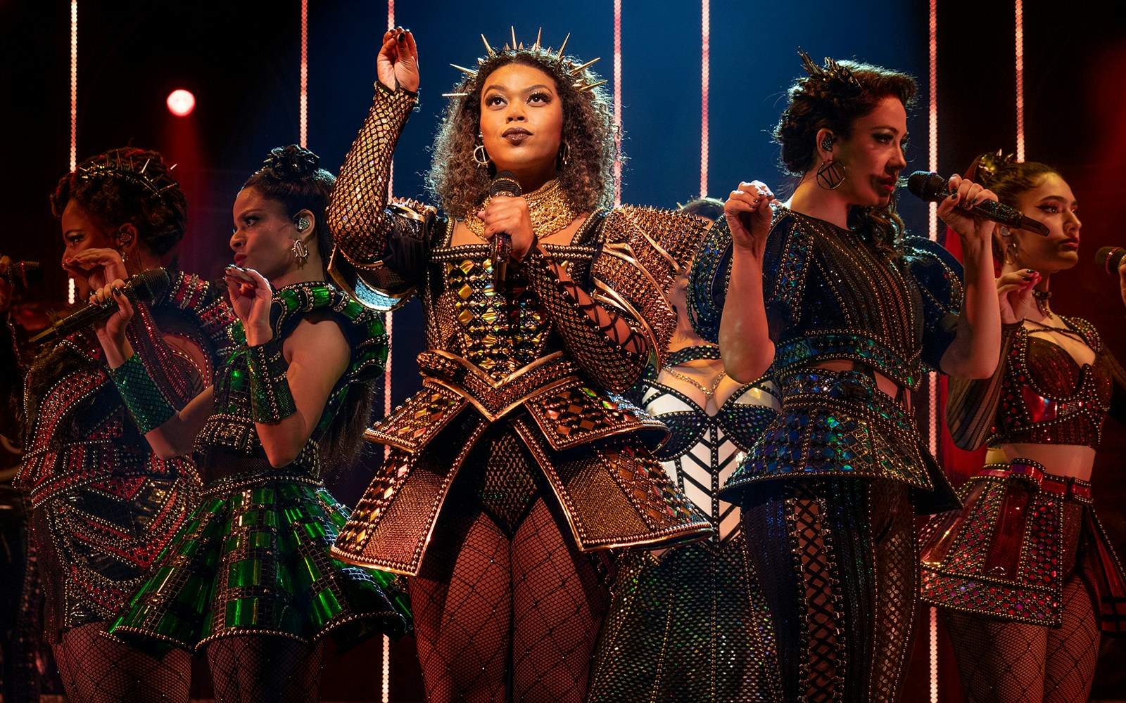 Performers in elaborate costumes singing on stage during SIX: The Musical.