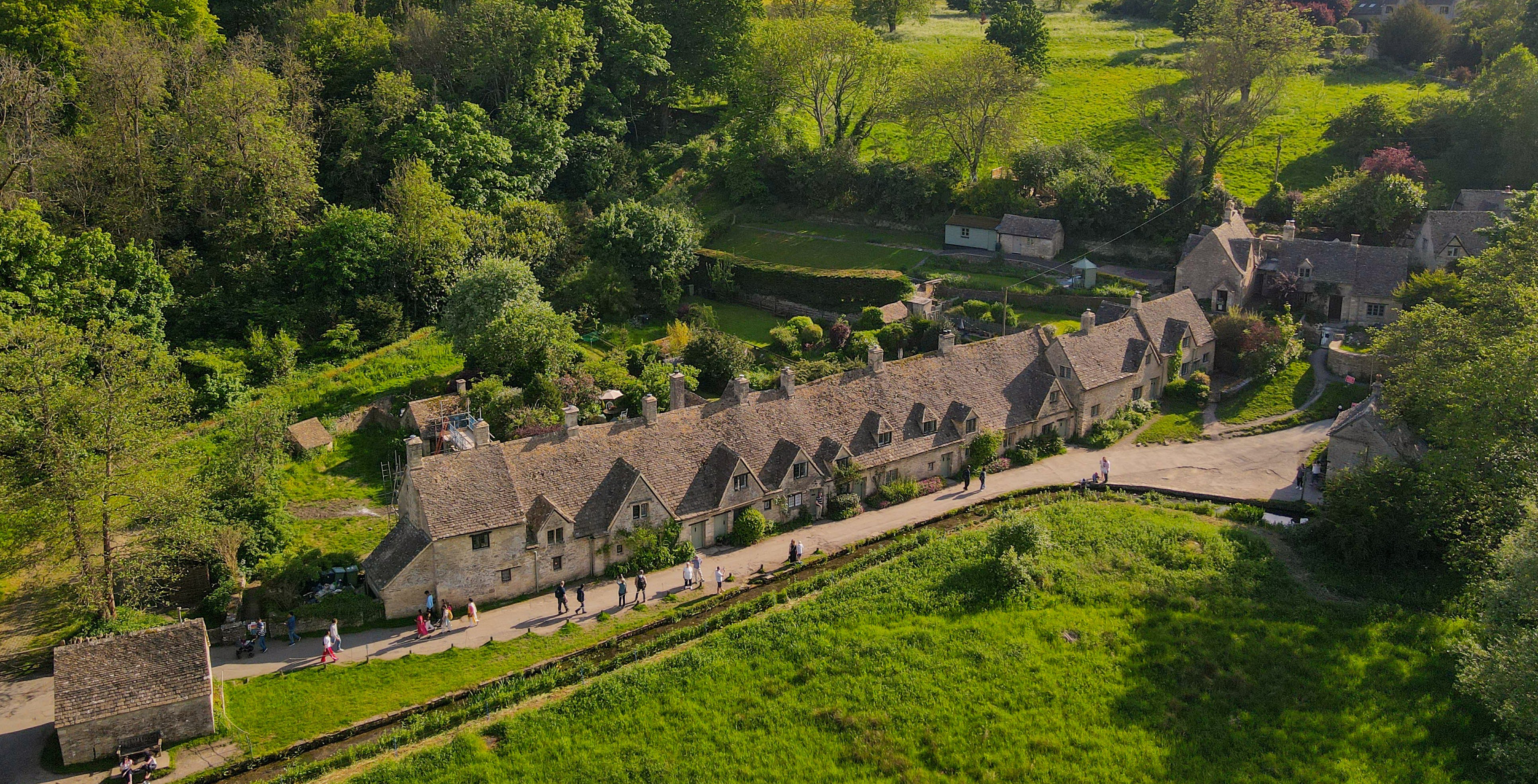Cotswold stone cottages in a lush green landscape with visitors walking along the path.
