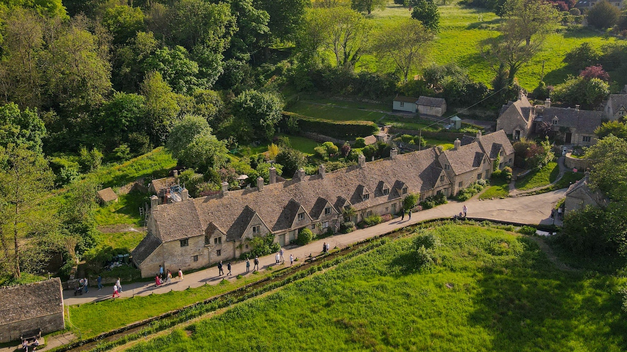 Cotswold stone cottages in a lush green landscape with visitors walking along the path.