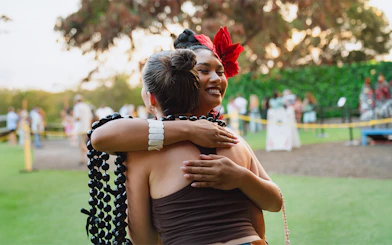 Guests embracing at Mauka Warriors Luau, Hawaii, with leis and traditional attire.