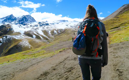 Hiker on trail with snow-capped mountains in Rainbow Mountain, Cusco.