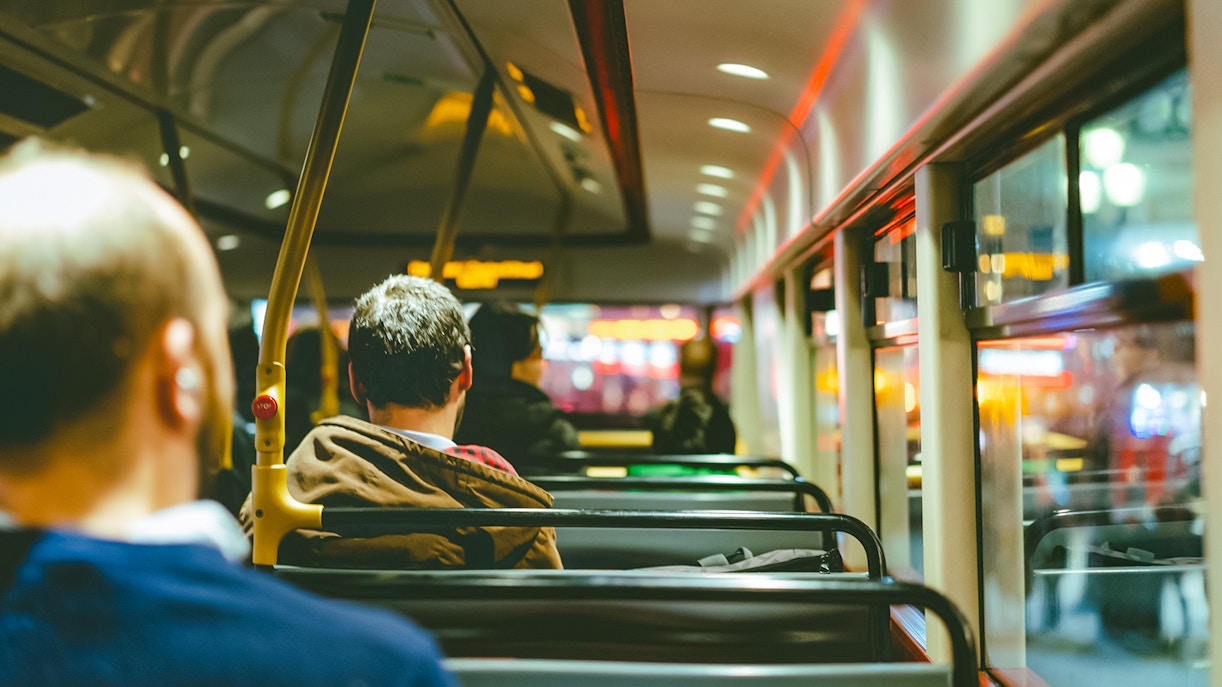 Passengers seated inside a bus at night with city lights visible through windows.