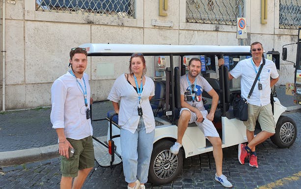 Tourists standing by a golf cart on a cobblestone street in Rome.