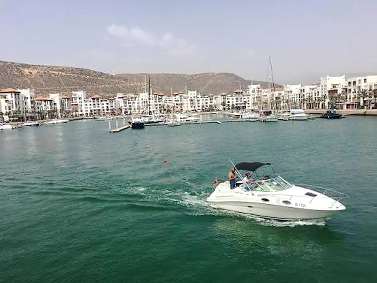 Boat cruising in Agadir marina with cityscape in the background, Morocco.