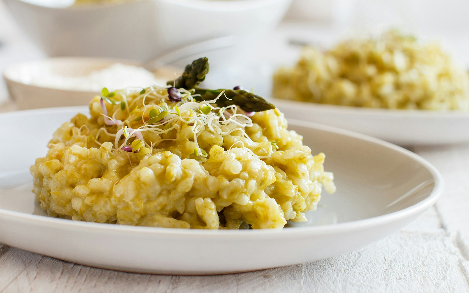 Creamy risotto garnished with asparagus and sprouts on a white plate.