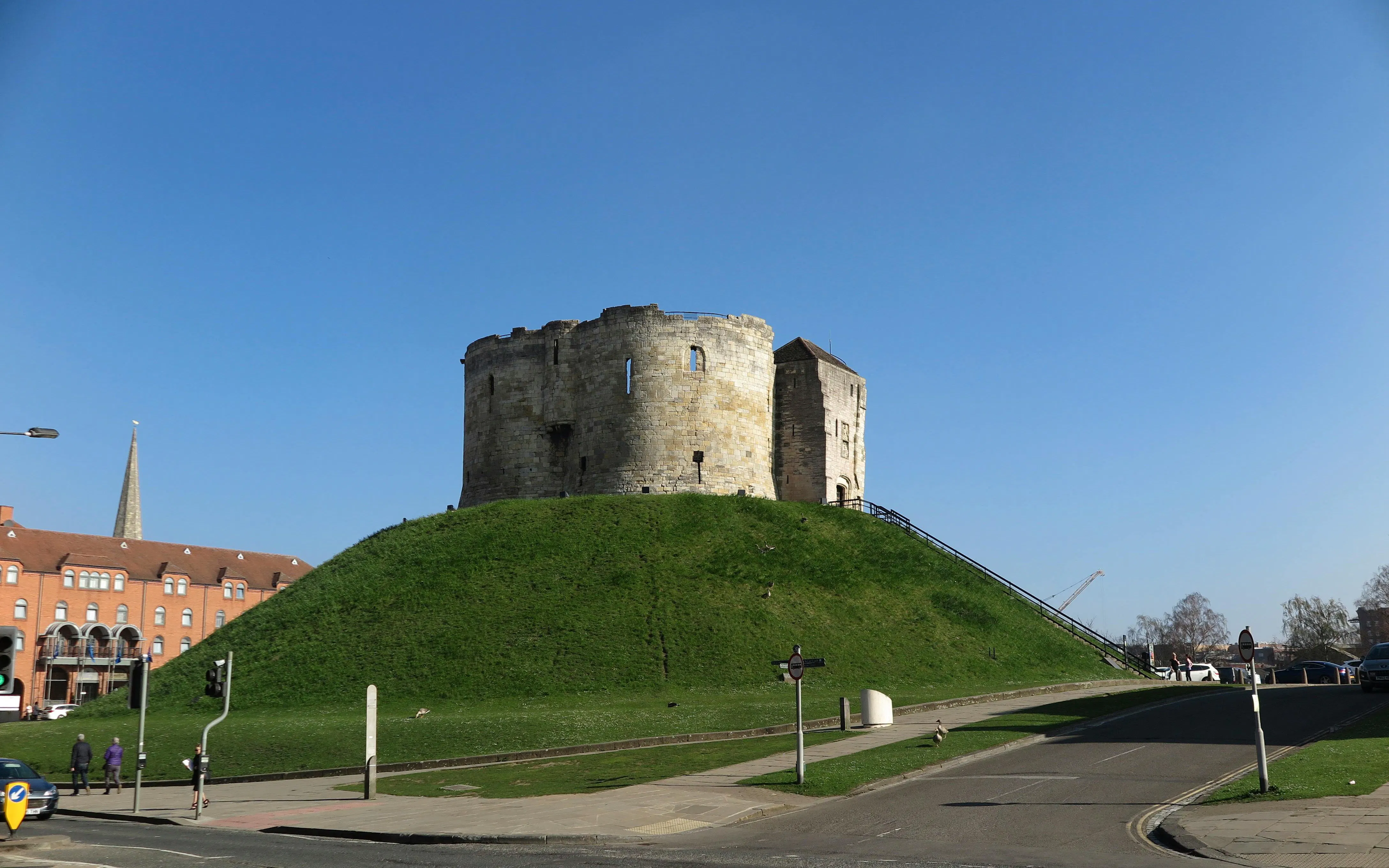 Clifford's Tower on a grassy hill in York, England, with clear blue sky.
