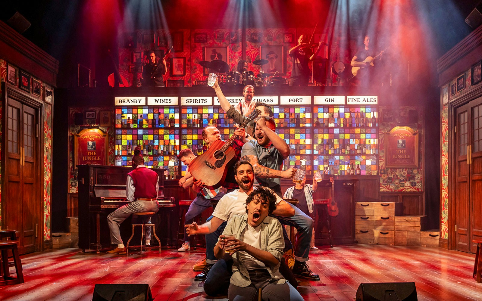 Performers on stage in The Choir of Man show, holding instruments and drinks.
