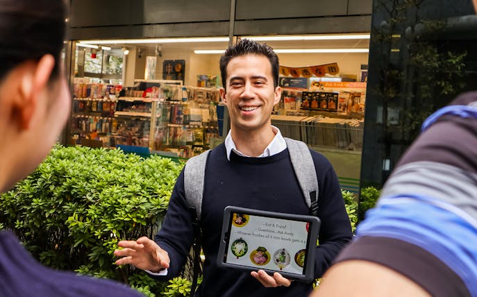 Tour guide holding a tablet during Tokyo Ramen Tasting Tour with 6 mini bowls of ramen.