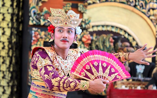 Balinese dancer performing at Garuda Wisnu Kencana at night, holding a decorative fan.