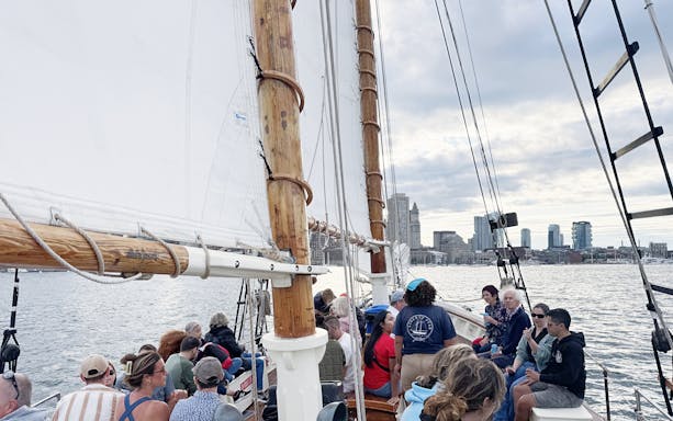 People sailing on the Liberty Star in Boston Harbor with city skyline in the background.