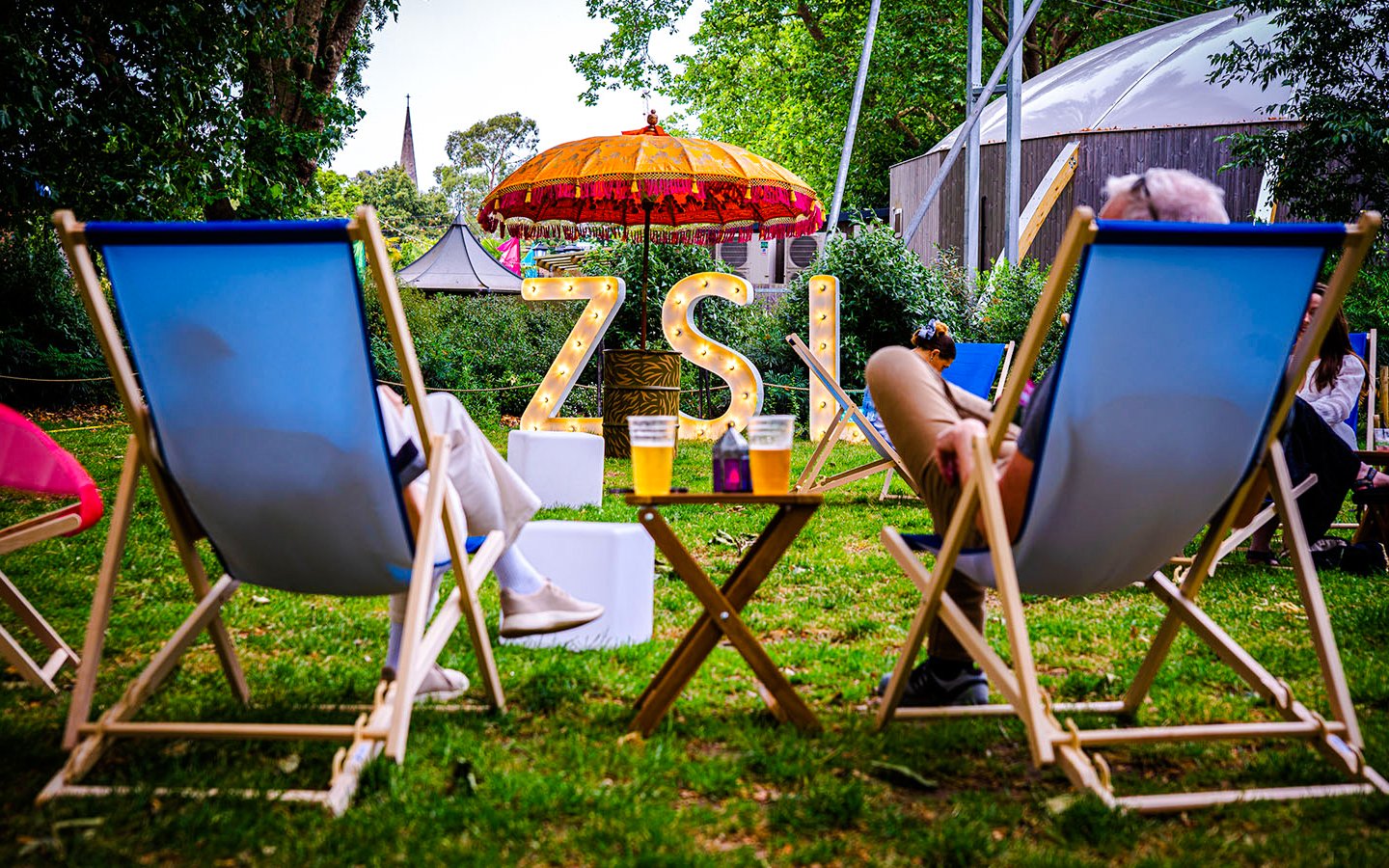 Guests relaxing in deck chairs at London Zoo after hours event.