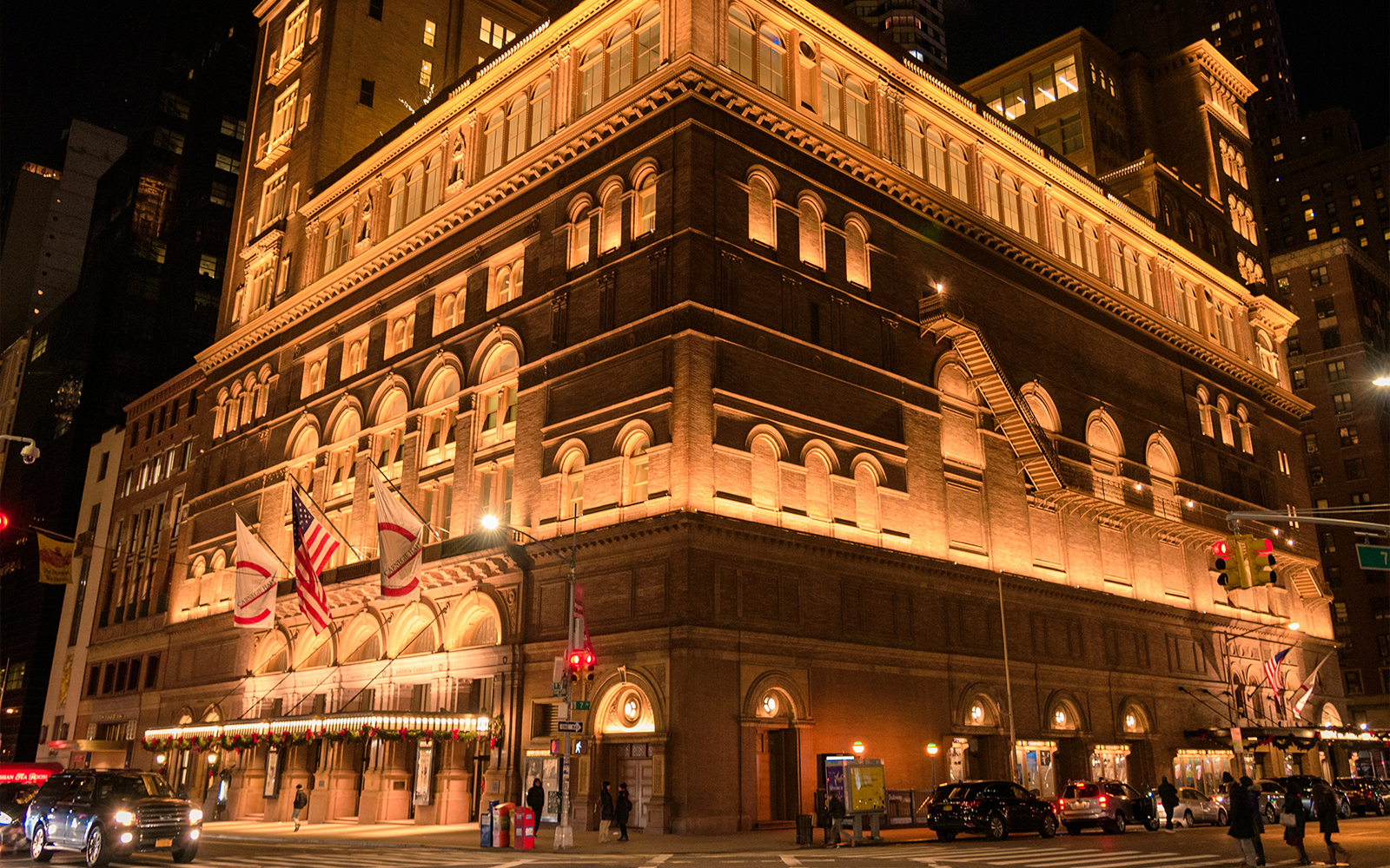 Carnegie Hall illuminated at night in New York City with flags and street view.