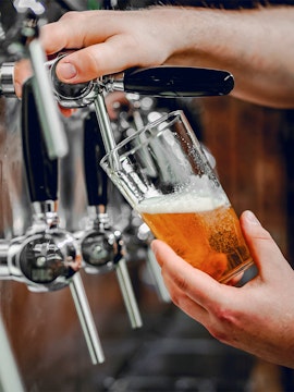 Hand pouring beer from tap into glass at a bar.