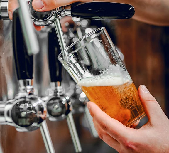 Hand pouring beer from tap into glass at a bar.