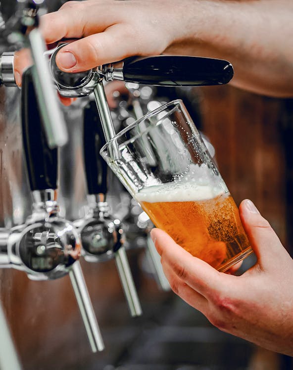 Hand pouring beer from tap into glass at a bar.