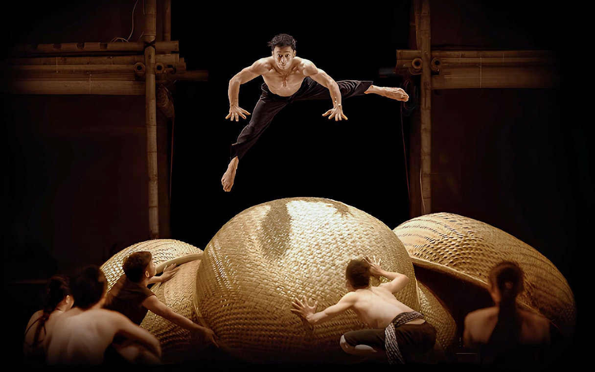 Acrobat leaping over large woven baskets at A O Show circus.