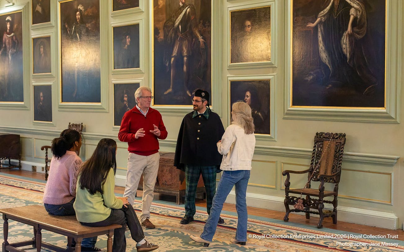 Tour group inside Palace of Holyroodhouse, viewing historic paintings with a guide.
