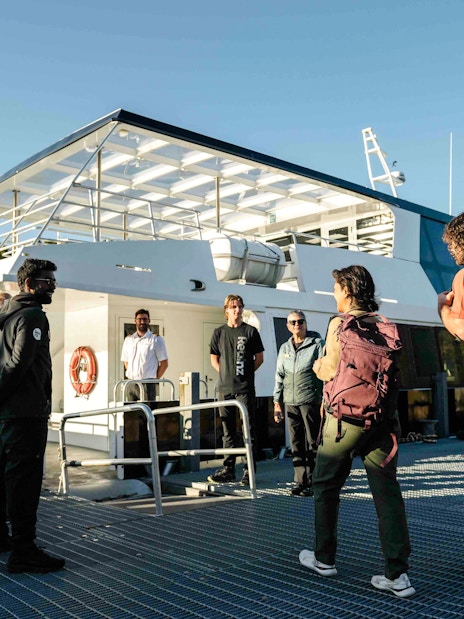 Passengers receive a briefing from the crew on the open deck of a boat in Doubtful Sound.