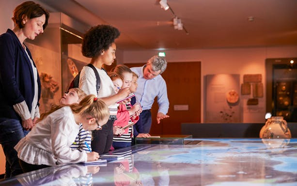 Group of children learning from an Egyptologist guide in a museum setting.