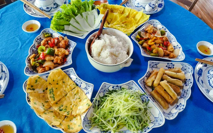 Vietnamese food platter with rice, spring rolls, pancakes, and stir-fried vegetables on a blue table.