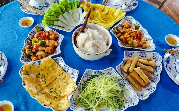 Vietnamese food platter with rice, spring rolls, pancakes, and stir-fried vegetables on a blue table.