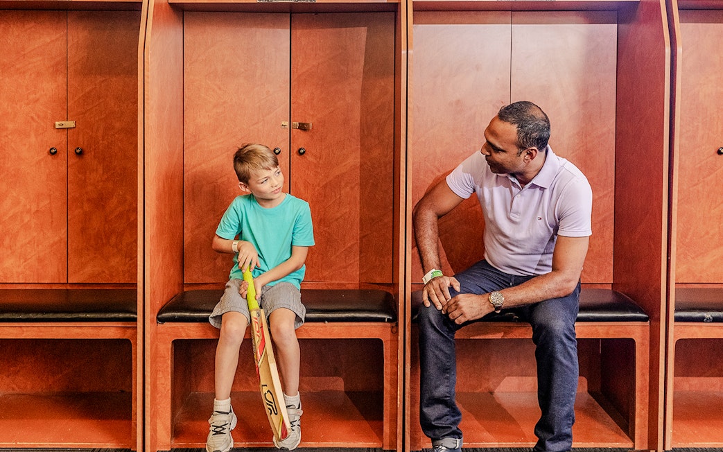 Tour group in Sydney Cricket Ground dressing room with guide and child holding cricket bat.