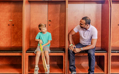 Tour group in Sydney Cricket Ground dressing room with guide and child holding cricket bat.