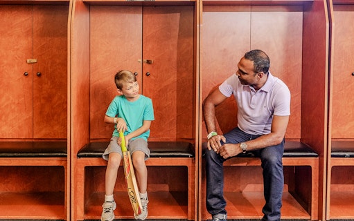 Tour group in Sydney Cricket Ground dressing room with guide and child holding cricket bat.