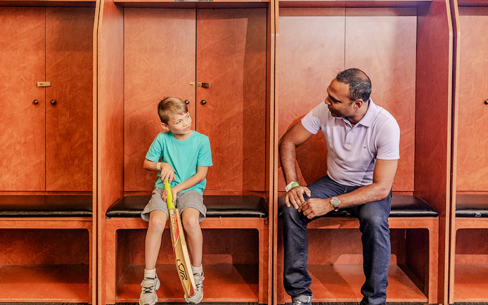 Tour group in Sydney Cricket Ground dressing room with guide and child holding cricket bat.