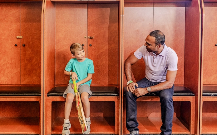Tour group in Sydney Cricket Ground dressing room with guide and child holding cricket bat.