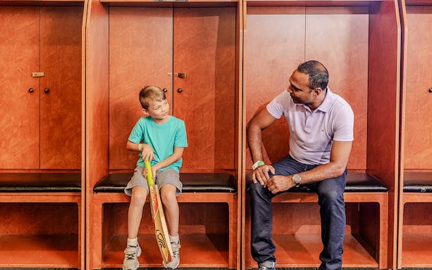 Tour group in Sydney Cricket Ground dressing room with guide and child holding cricket bat.