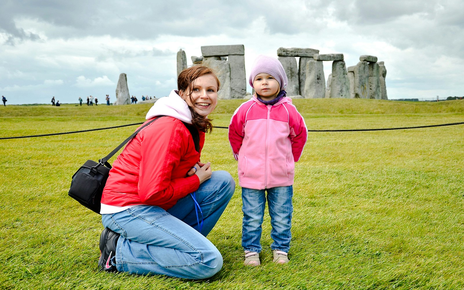 Child and adult at Stonehenge with ancient stones in the background.