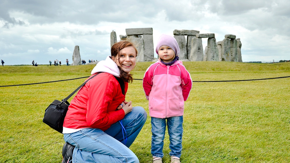 Child and adult at Stonehenge with ancient stones in the background.