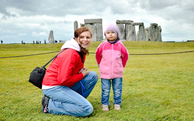 Child and adult at Stonehenge with ancient stones in the background.