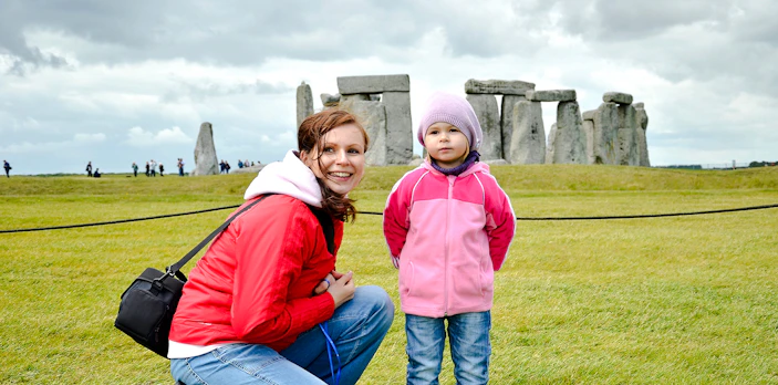 Child and adult at Stonehenge with ancient stones in the background.