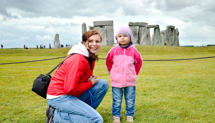 Child and adult at Stonehenge with ancient stones in the background.