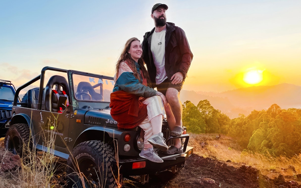 Couple sitting on a jeep during a Black Lava Exploration tour in Bali at sunset.