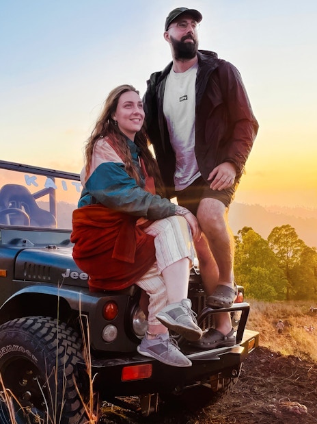 Couple sitting on a jeep during a Black Lava Exploration tour in Bali at sunset.