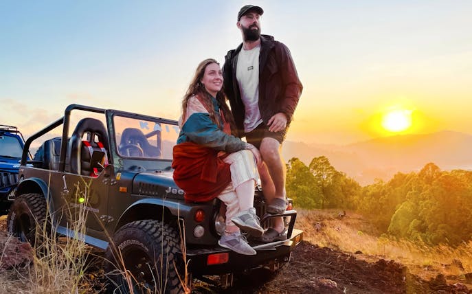 Couple sitting on a jeep during a Black Lava Exploration tour in Bali at sunset.
