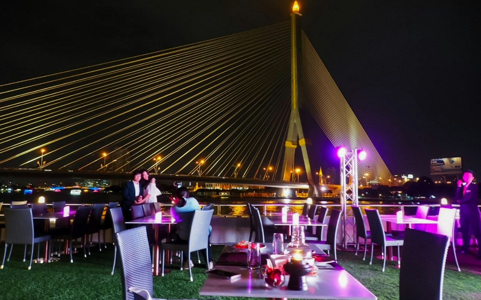 Rama VIII Bridge view from a riverside dining area at night in Bangkok, Thailand.
