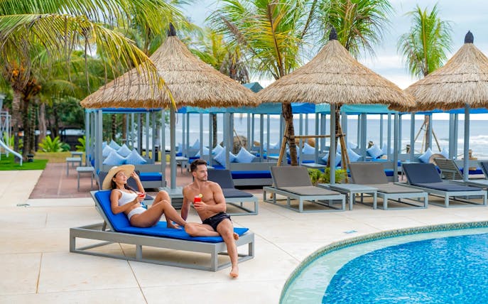 Couple relaxing by the pool at Flamingo Beach Club with tropical cabanas and palm trees.