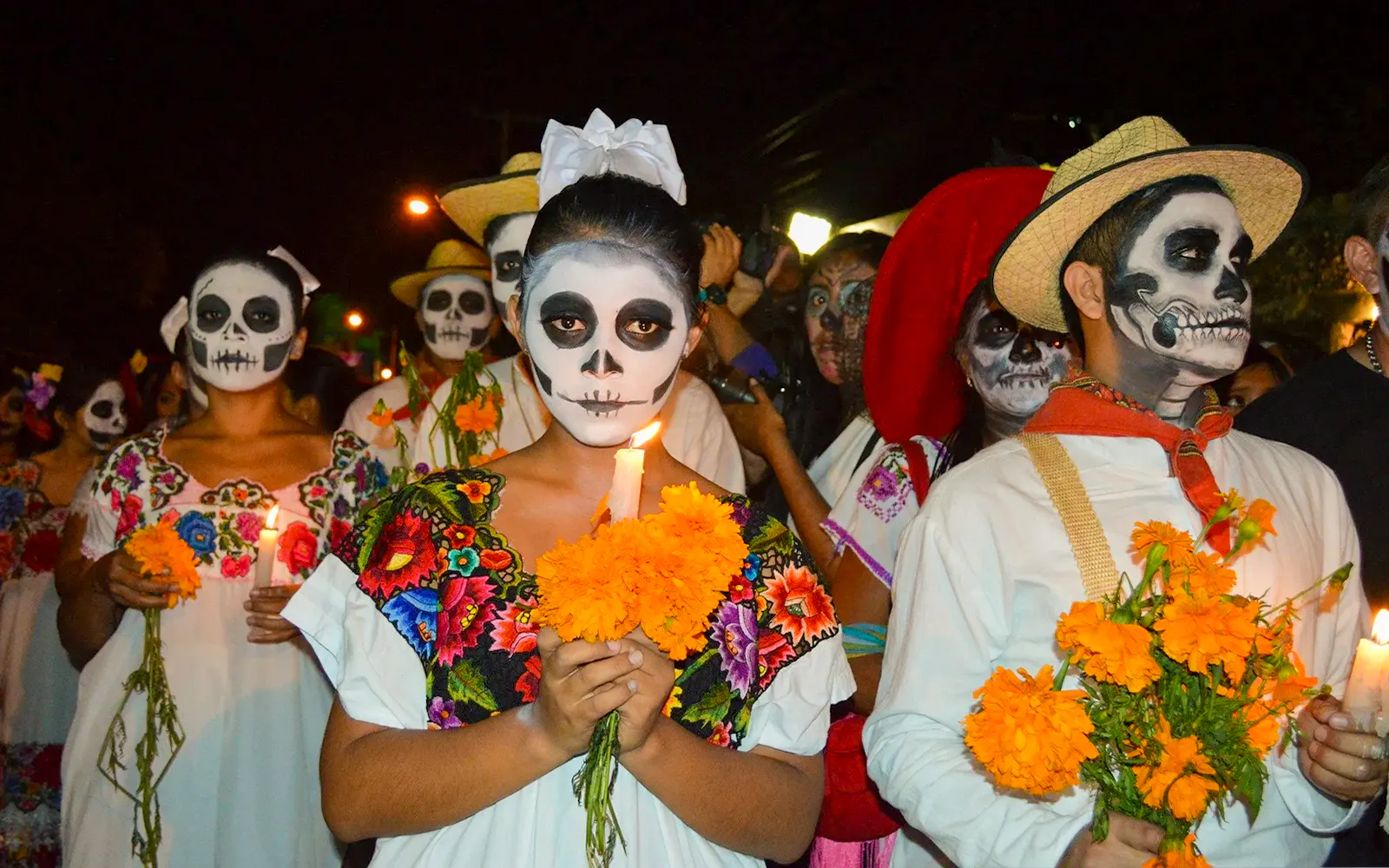 Participants in traditional face paint and costumes holding marigolds during Day of the Dead march, Mexico.