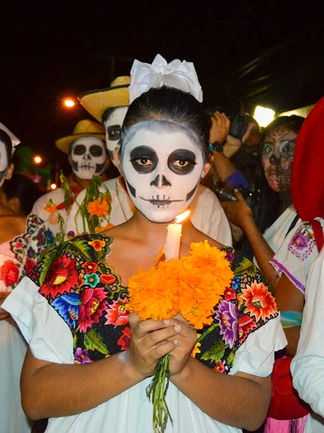 Participants in traditional face paint and costumes holding marigolds during Day of the Dead march, Mexico.