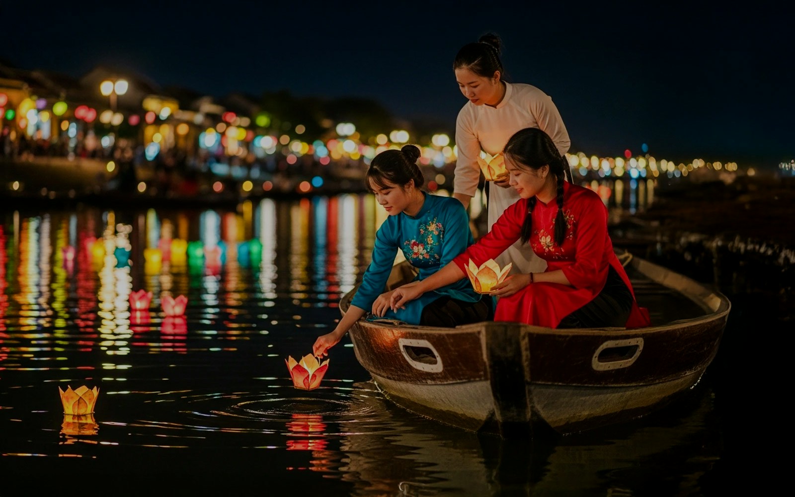 Tourists in a boat releasing lanterns on Hoi An River at night.