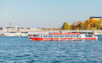 Stockholm sightseeing boat on water near cityscape and bridge.
